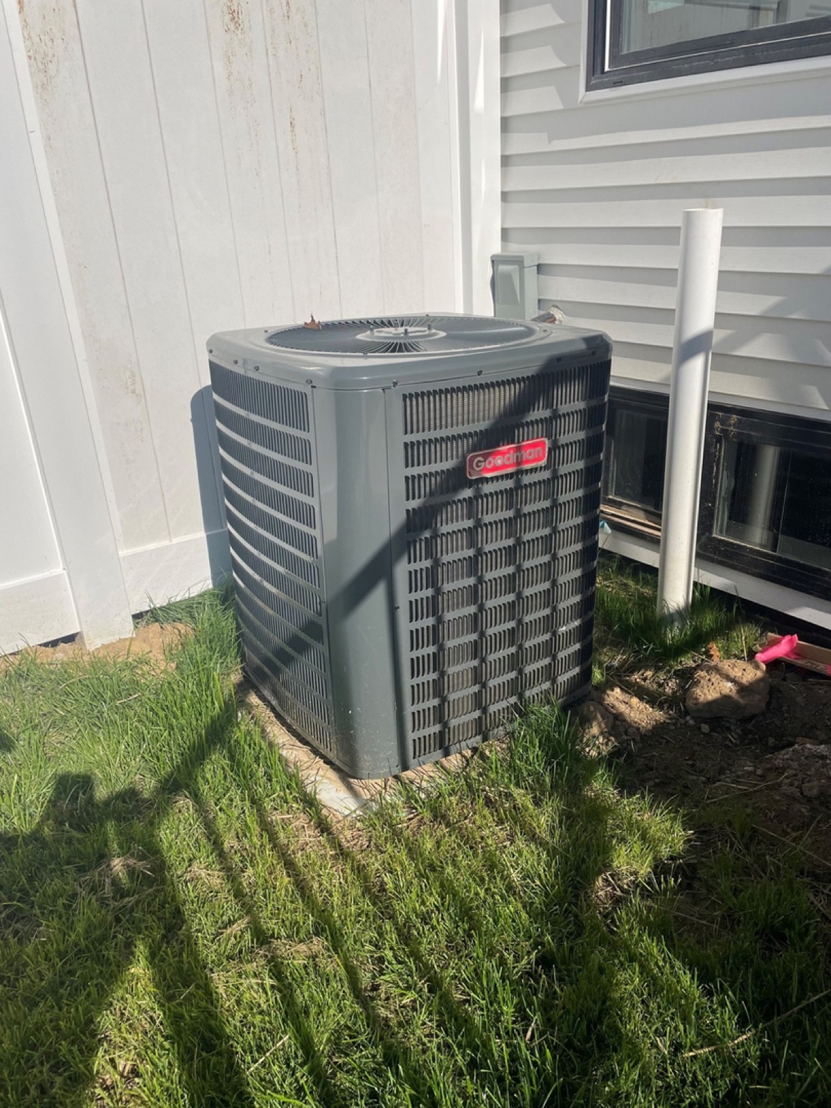 Freshly installed Goodman condenser on a new pad by a white-sided home