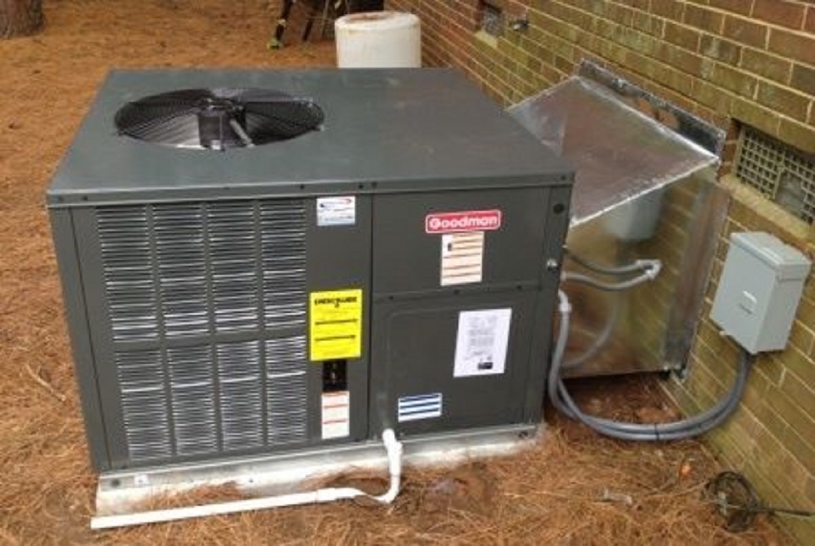 Goodman packaged HVAC unit with new ductwork installed beside a brick home
