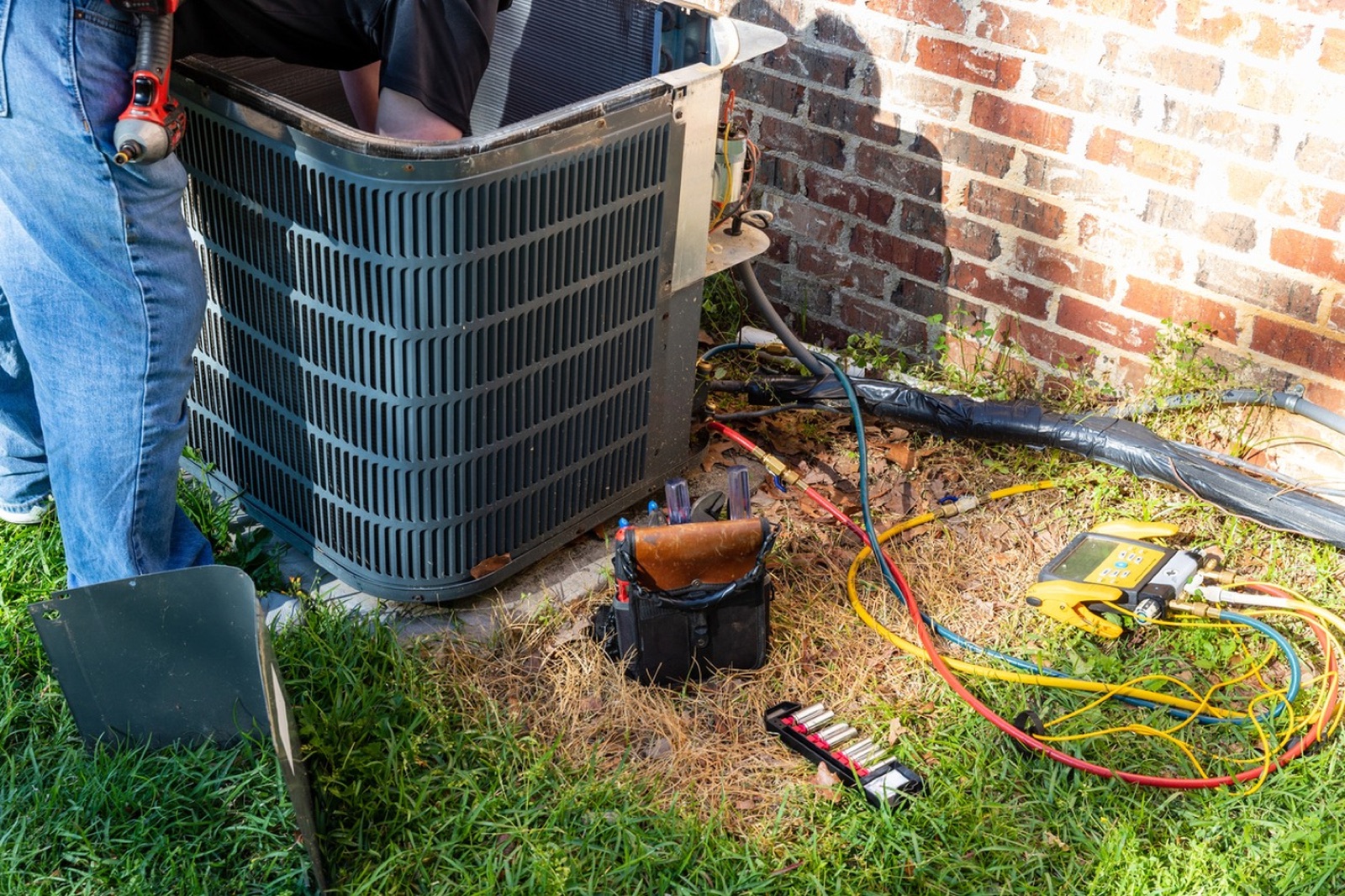 Climate Mechanics technician servicing an outdoor AC unit with refrigerant gauges